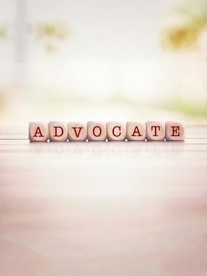 The word ADVOCATE spelled with wooden letter cubes, representing caregiving, self-care, and empowerment through advocacy.
