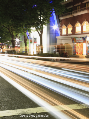 City street at night with blurred lights rushing by, symbolizing life’s constant motion and the reminder to pause and check what’s driving you — fear or curiosity. Image for Care & Glow Collective blog post about slowing down, awareness, and mindful movement